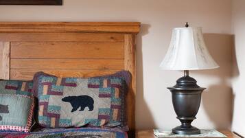 Un dormitorio con cabecera de madera, colcha acolchada, dos almohadas decorativas, una lámpara de noche y una mesita de noche de madera con cajón.