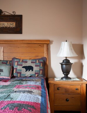 Une chambre à coucher avec une tête de lit en bois, une couvre-lit matelassée, deux coussins décoratifs, une lampe de chevet et une petite table de chevet en bois avec un tiroir.