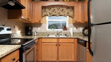 A kitchen with wooden cabinets, a stainless steel refrigerator, a stove, and a window with a rooster-themed curtain.