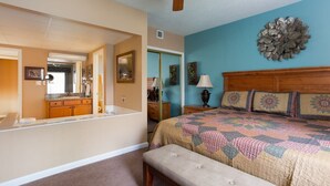Une chambre à coucher comprenant un lit, un banc, un ventilateur de plafond, un miroir et une porte donnant sur une autre pièce.