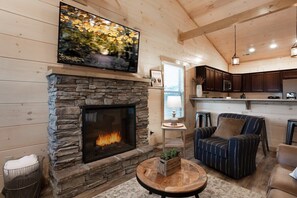 Una sala de estar acogedora con chimenea de piedra, un televisor montado encima y un espacio de descanso cómodo con sillones a rayas.