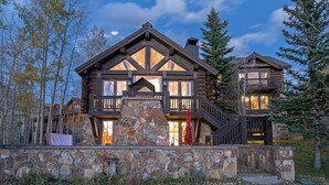 A log cabin with a stone foundation, wooden balconies, and a stone staircase leading to the entrance.