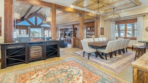 A spacious dining area with a wooden table and chairs, surrounded by bookshelves and a large window with curtains.
