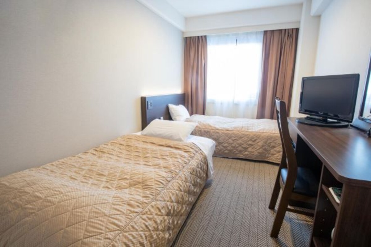Una habitación de hotel con dos camas, un escritorio y una televisión.