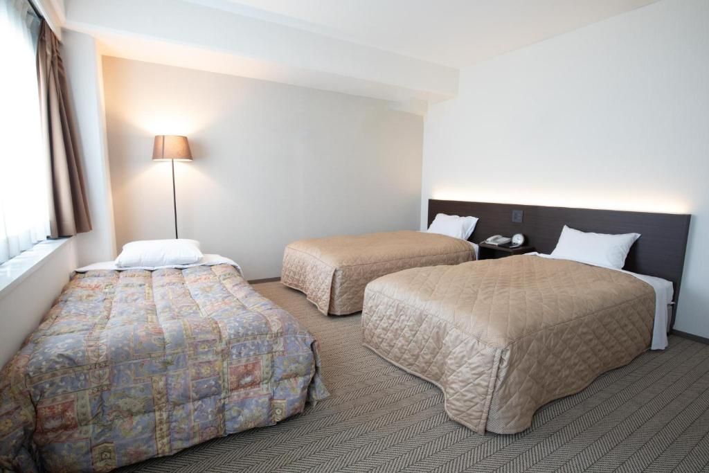 A hotel room with two beds, a nightstand, a lamp, and a window with curtains.
