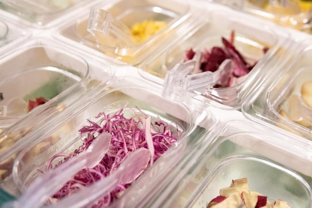 Multiple clear plastic containers with various food items and garnishes.