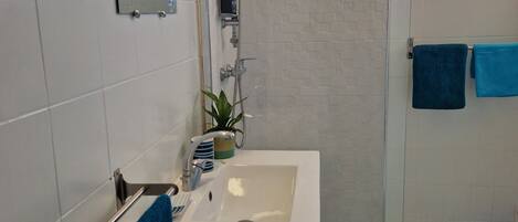 A modern bathroom with a shower, sink, and a small window.