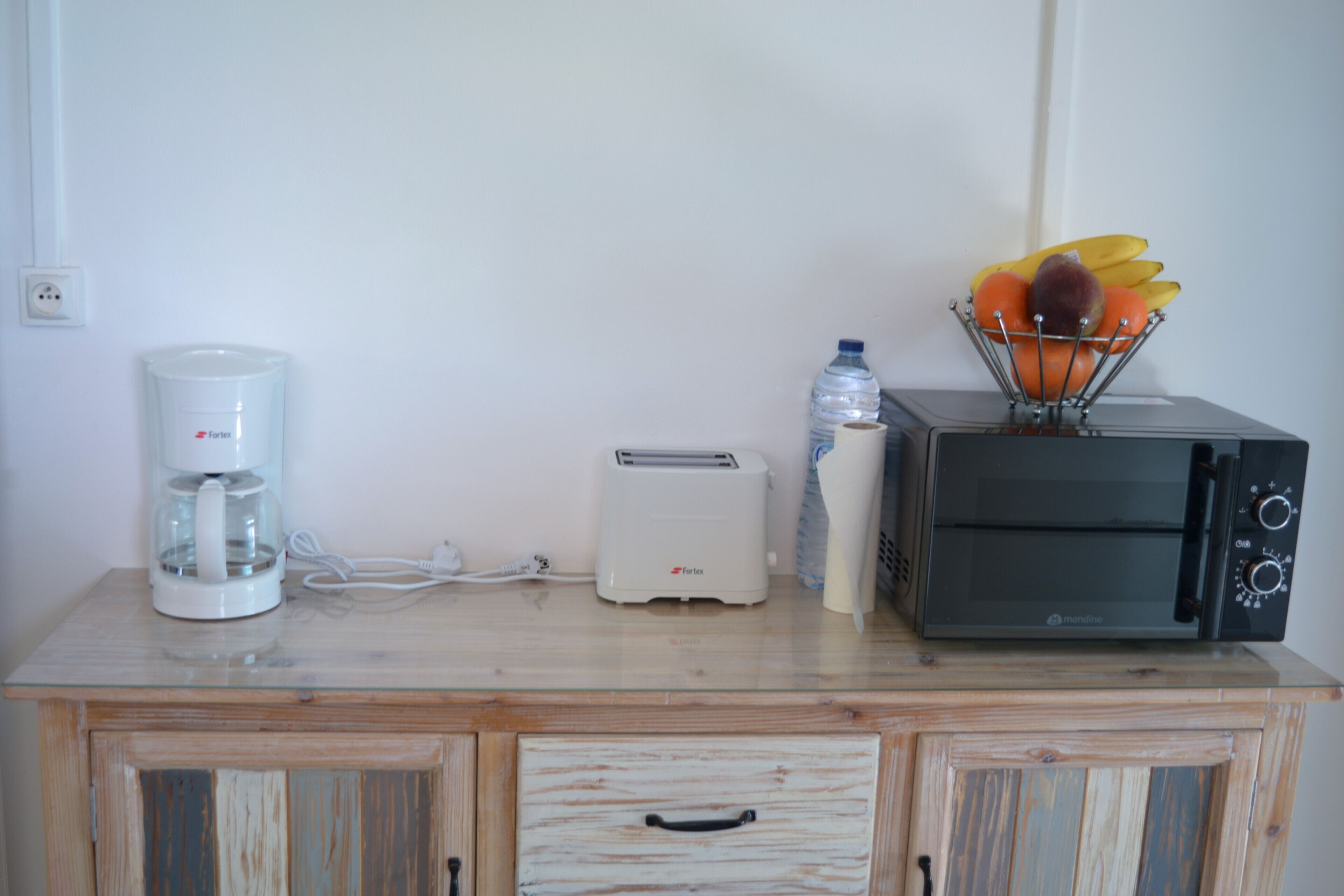 A kitchenette with a coffee maker, toaster, microwave, and a fruit basket on a wooden countertop.