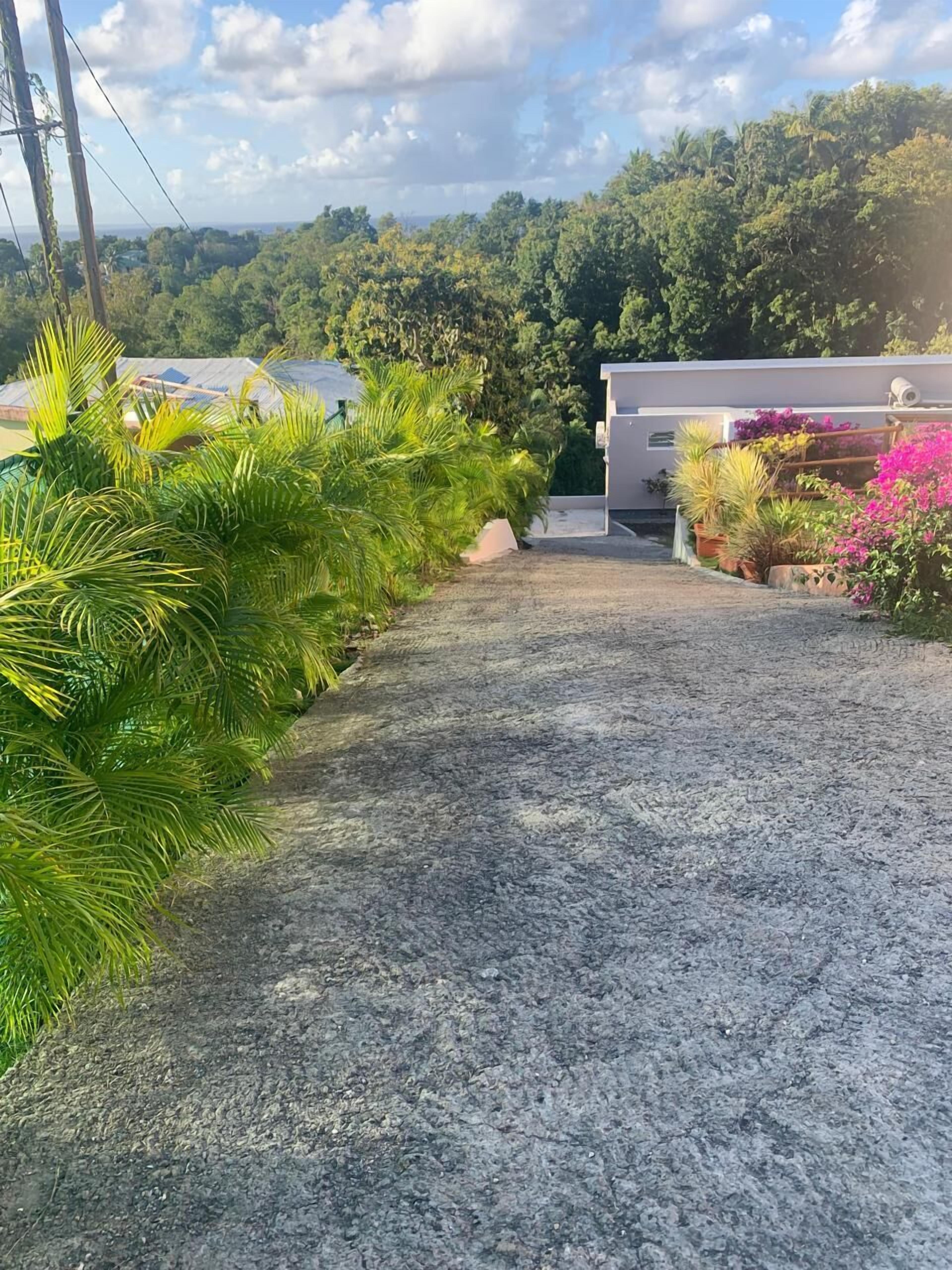 A gravel pathway leading to a building with a view of a lush green hillside.