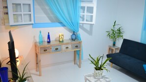 Ein Wohnzimmer mit einem dunklen Sofa, einem hölzernen Beistelltisch, einem kleinen weißen Tisch und einem blauen Vorhang.