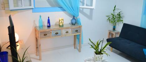A living room with a dark sofa, a wooden side table, a small white table, and a blue curtain.