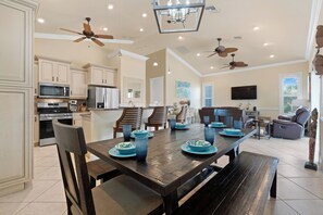 A spacious kitchen with modern appliances, a dining area with a wooden table and blue dinnerware, and a living room with a television and comfortable seating.