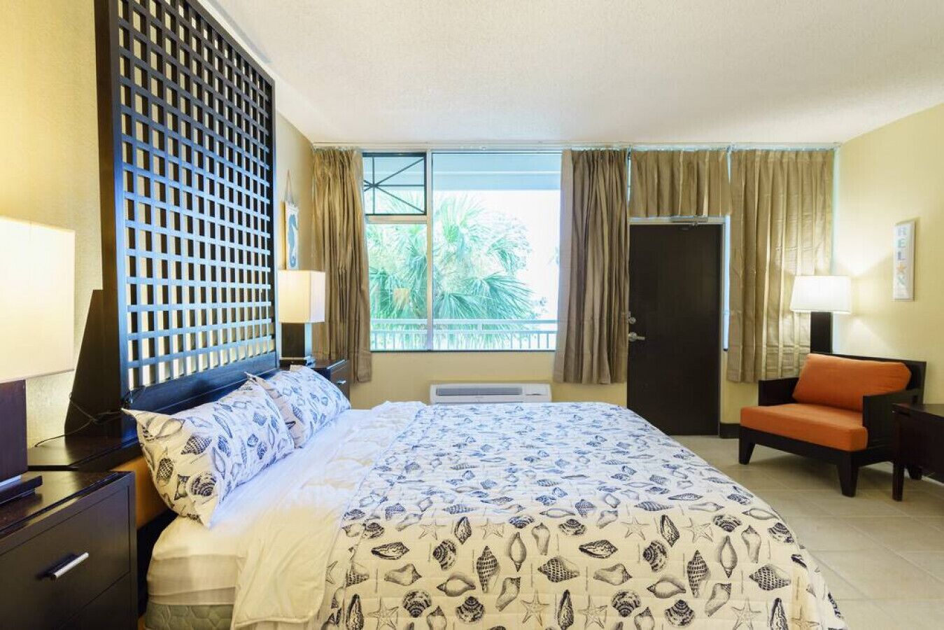 A hotel room with a bed, a chair, a desk, and a window with curtains.