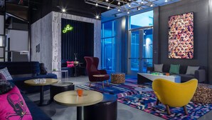 A modern lounge area with a dark blue sofa, a yellow armchair, and a red chair. There are round tables and a patterned rug. - Aloft by Marriott Savannah Airport (Pooler)