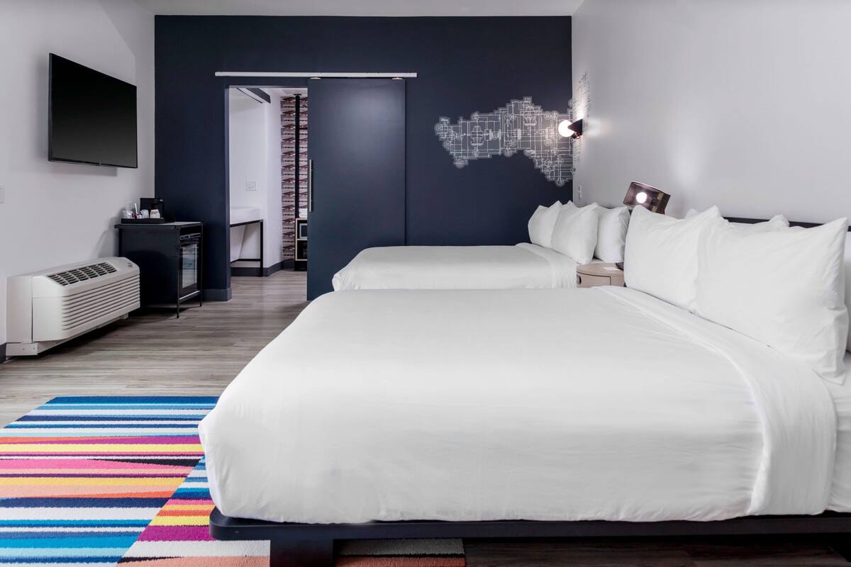 A modern hotel room with two beds, a large mirror, a flat-screen TV, and a map artwork on the wall.
