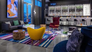 A modern lounge area with a bar, seating, and a large abstract painting. - Aloft by Marriott Savannah Airport (Pooler)