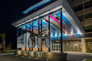 A modern hotel with a large illuminated 'HOTELS' sign, large windows, and a contemporary design. - Aloft by Marriott Savannah Airport (Pooler)