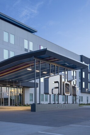 A modern hotel entrance with a large sign, covered walkway, and glass doors.
