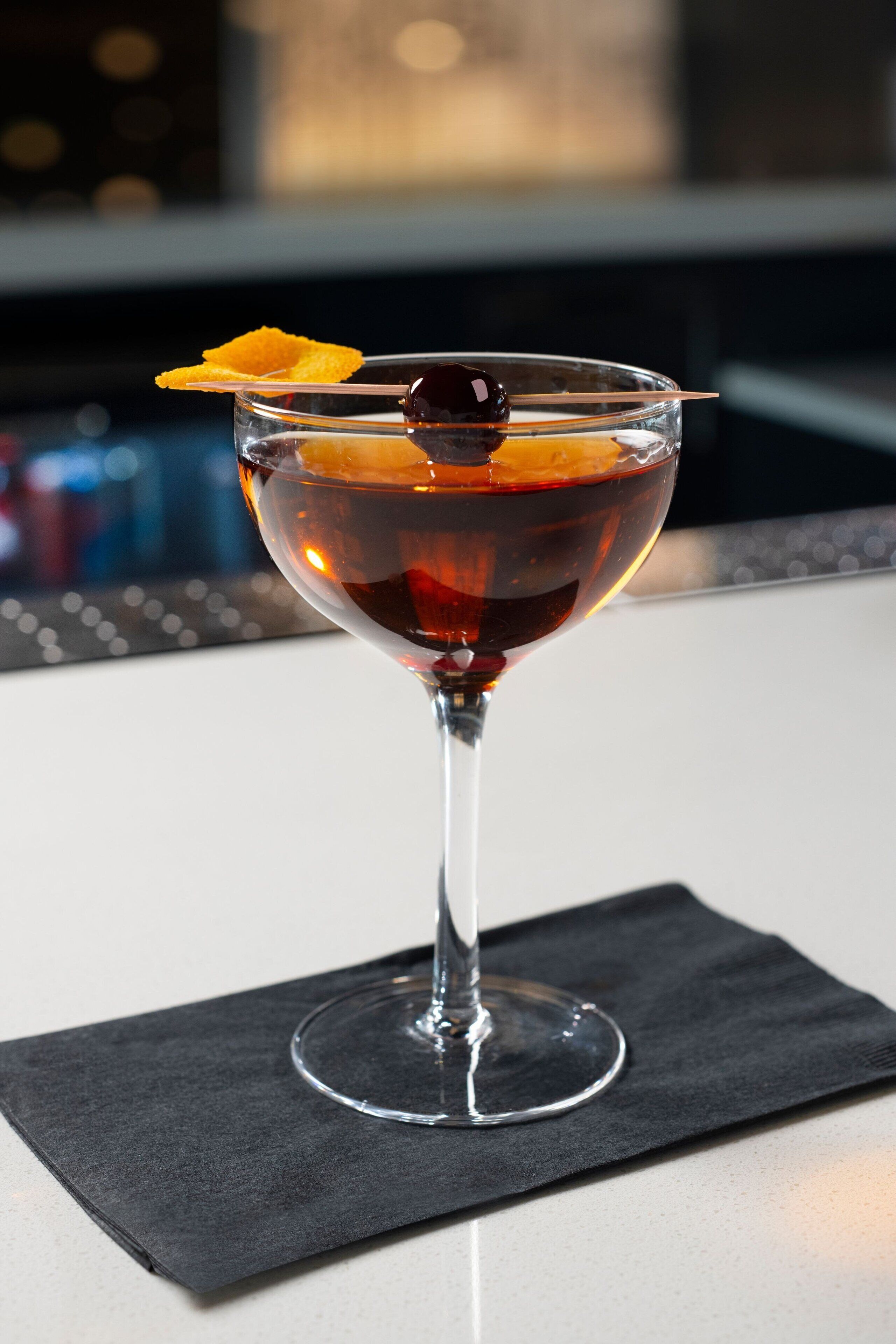 Ein Cocktail im Stielglas mit Orangenzesten auf einer schwarzen Serviette.