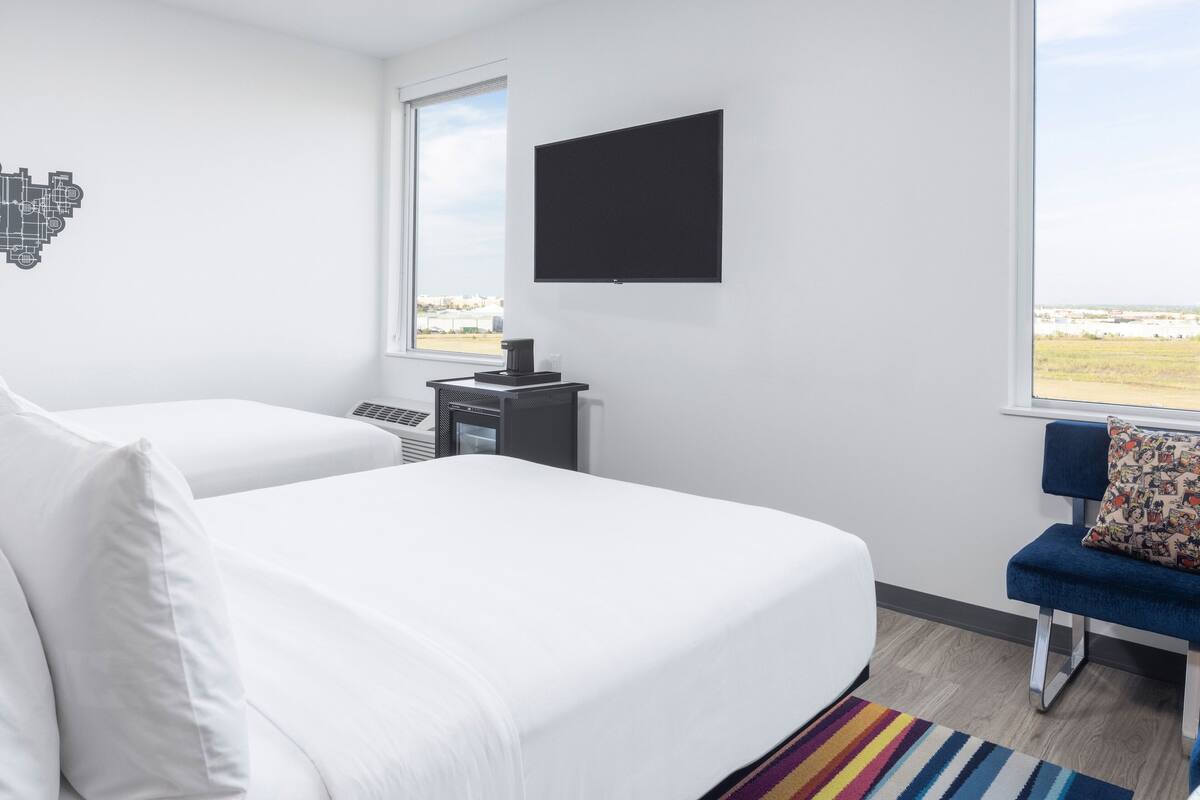 Une chambre d’hôtel avec deux lits, un téléviseur fixé au mur, un bureau avec un ordinateur et une vue sur le paysage par la fenêtre.