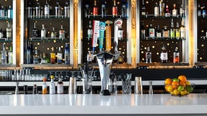 Una zona de bar con varias estanterías llenas de botellas de licor, una grifería central y un frutero en la barra.