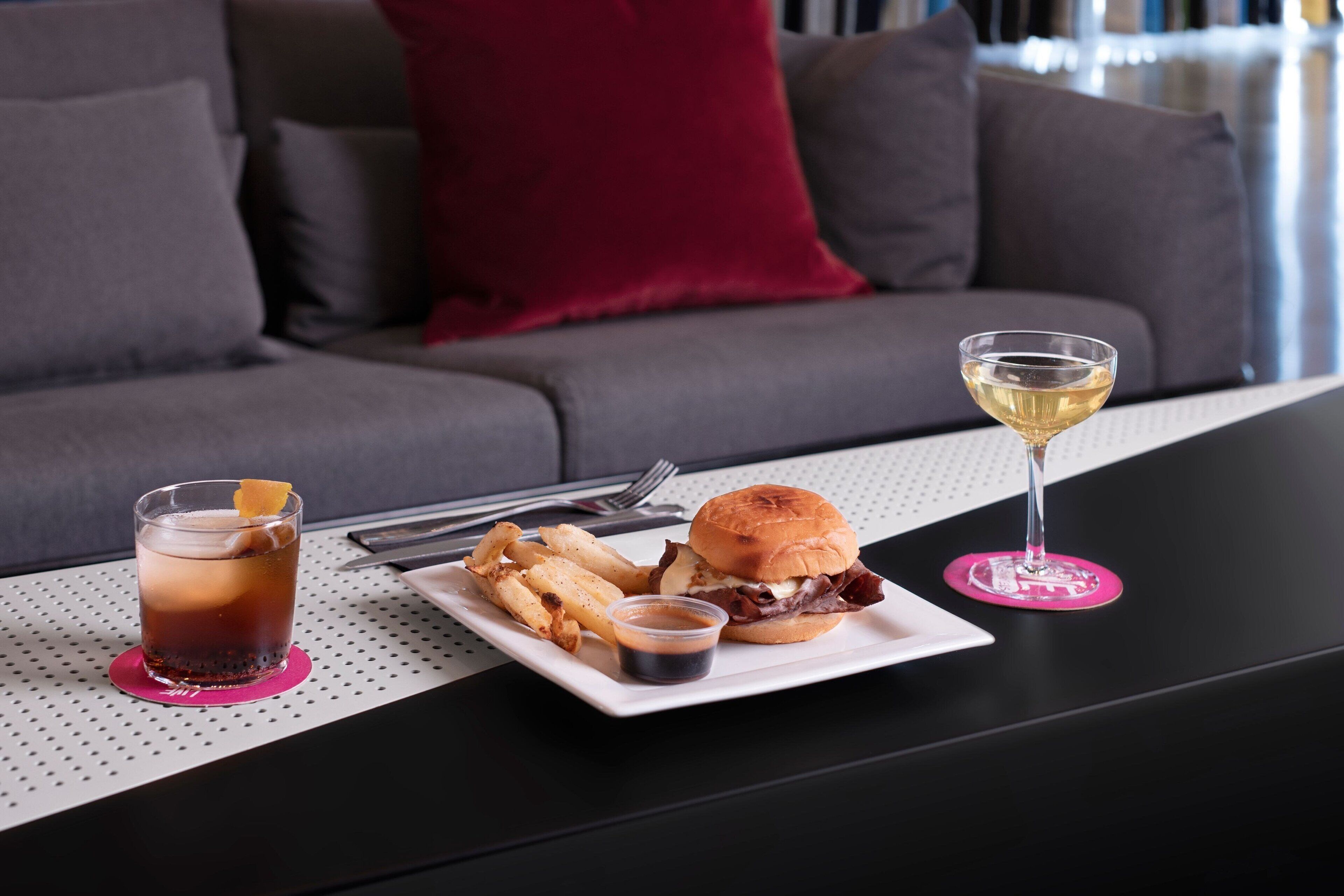 A dining table with a burger, fries, a drink, and a glass of wine.