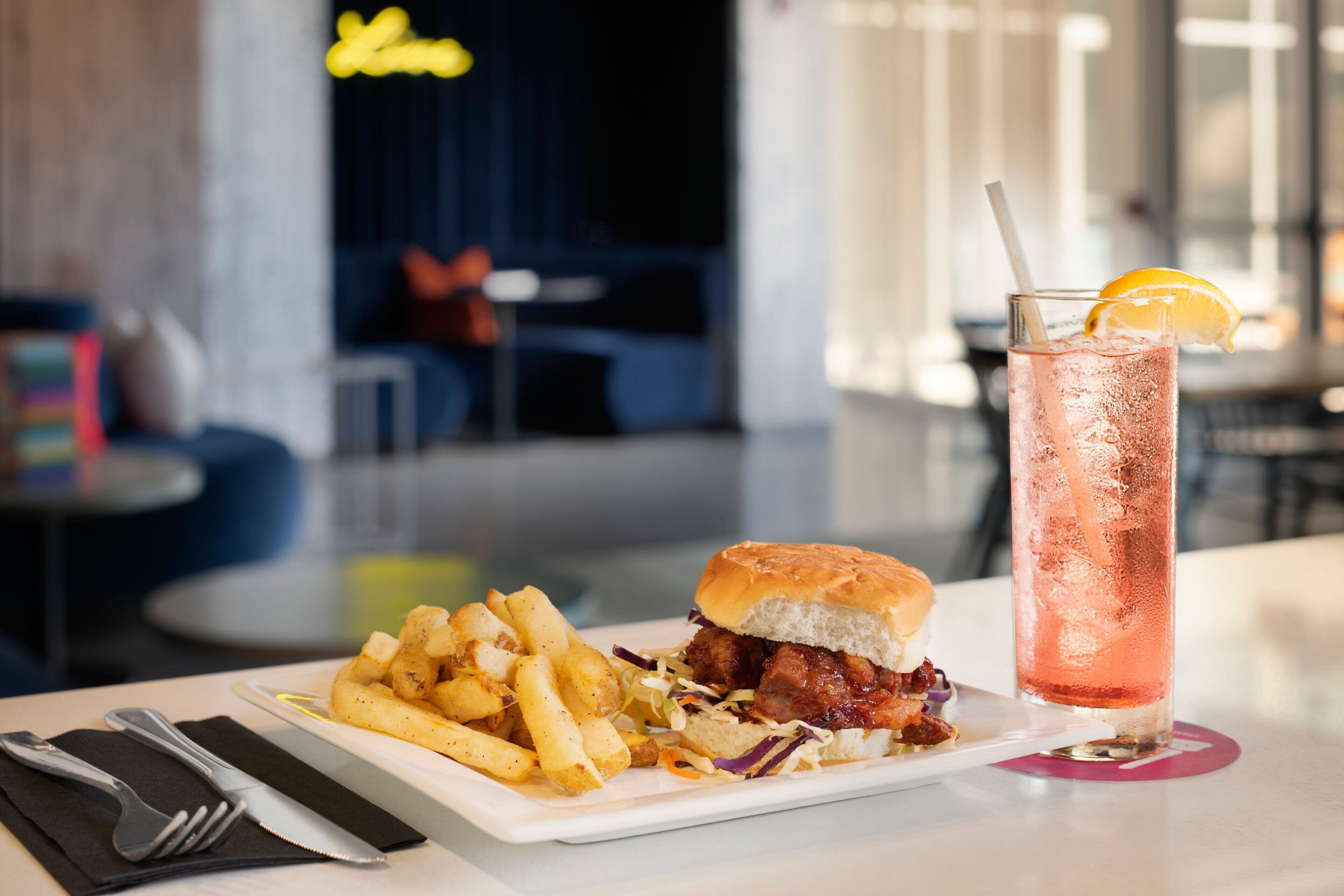 Ein Essen mit einem Burger, Pommes und einem Getränk auf einem Tisch in einem modernen Essbereich.