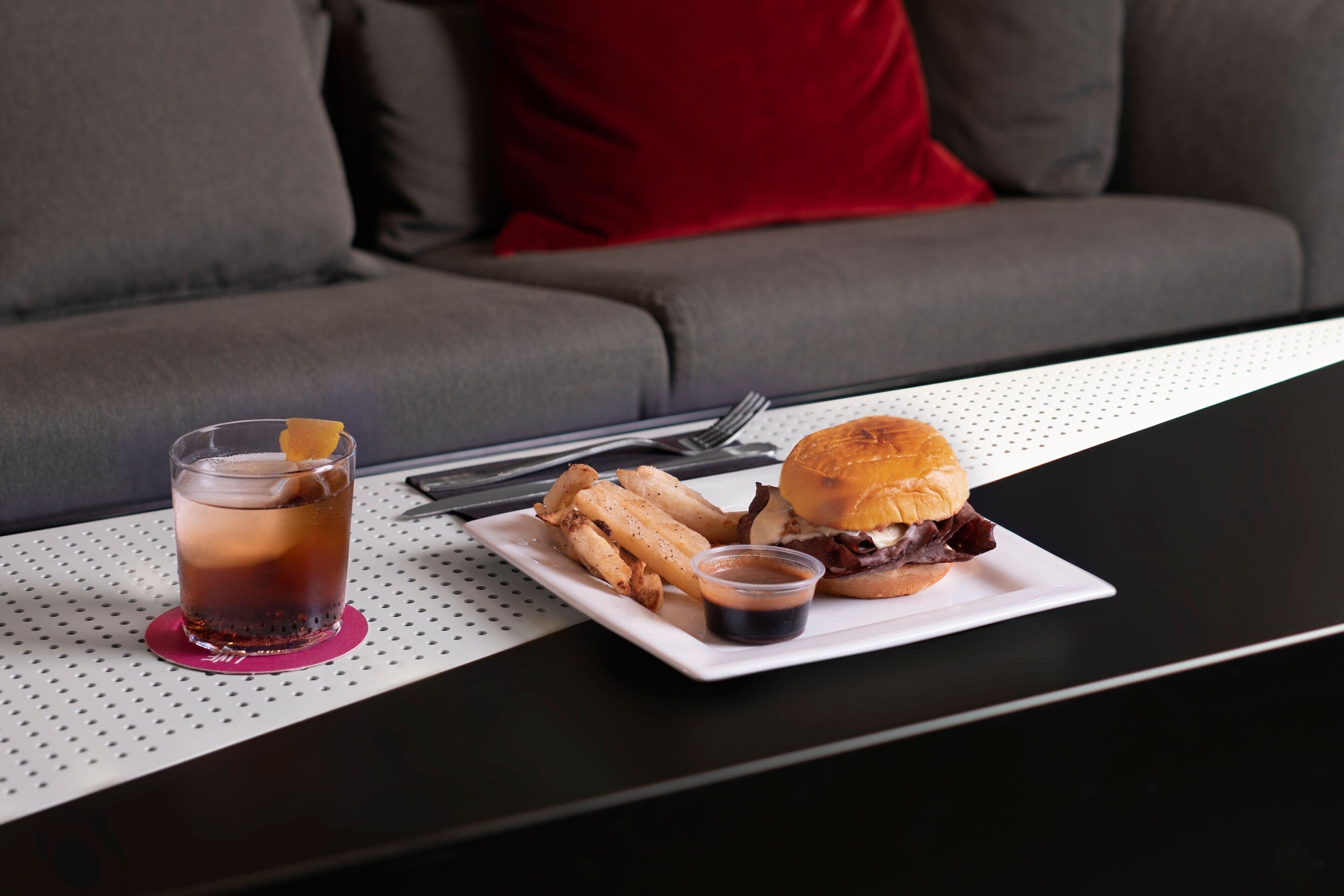 Un plato con una hamburguesa y papas fritas, una bebida en un vaso y una servilleta sobre la mesa.