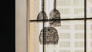 A modern living room with a large window, a black chair, a round table, and a hanging light fixture. - The Cloud One New York-Downton, part of the Motel One Group (New York)