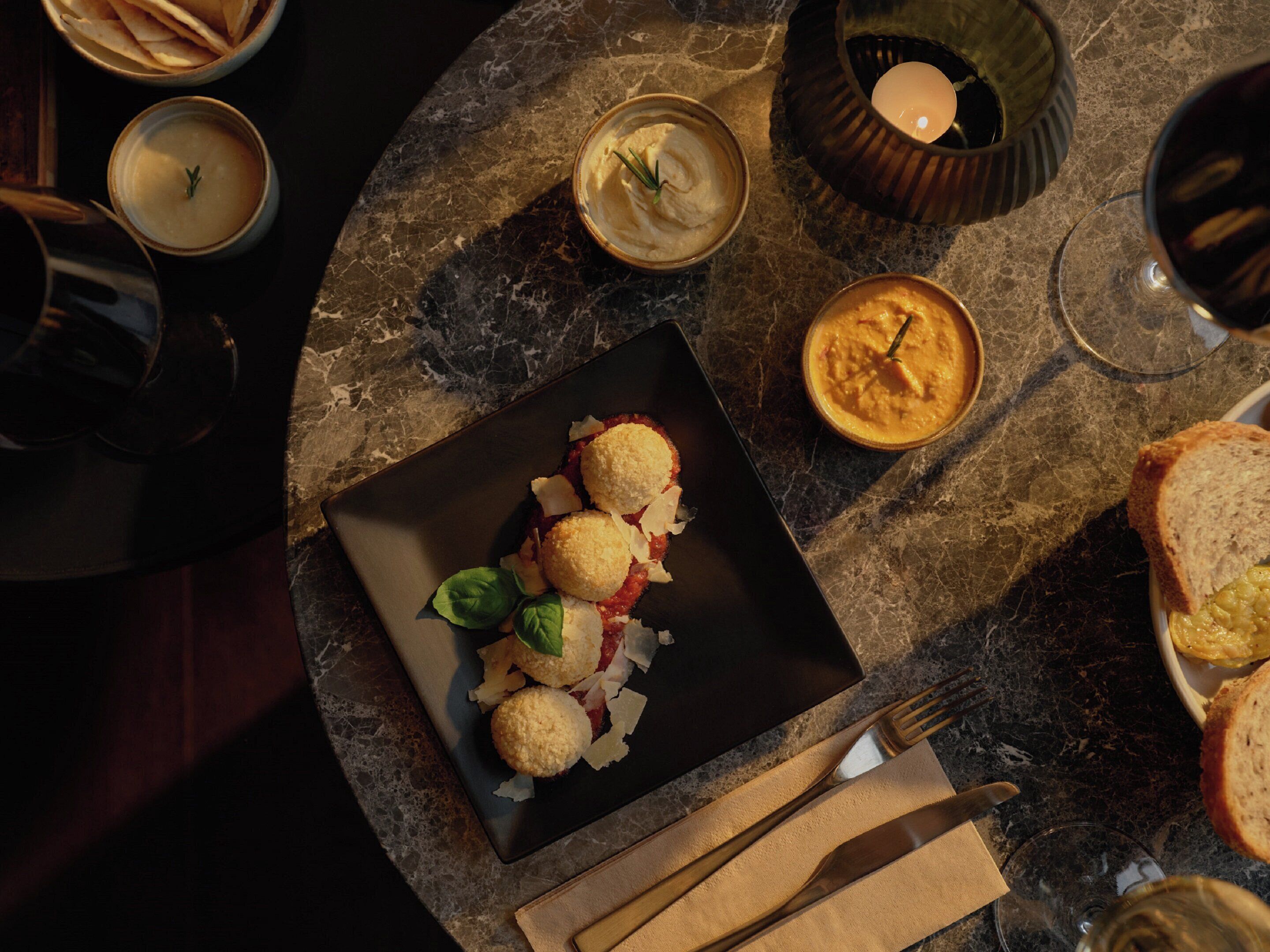 A dining table with a black plate of food, candles, and glasses of wine.