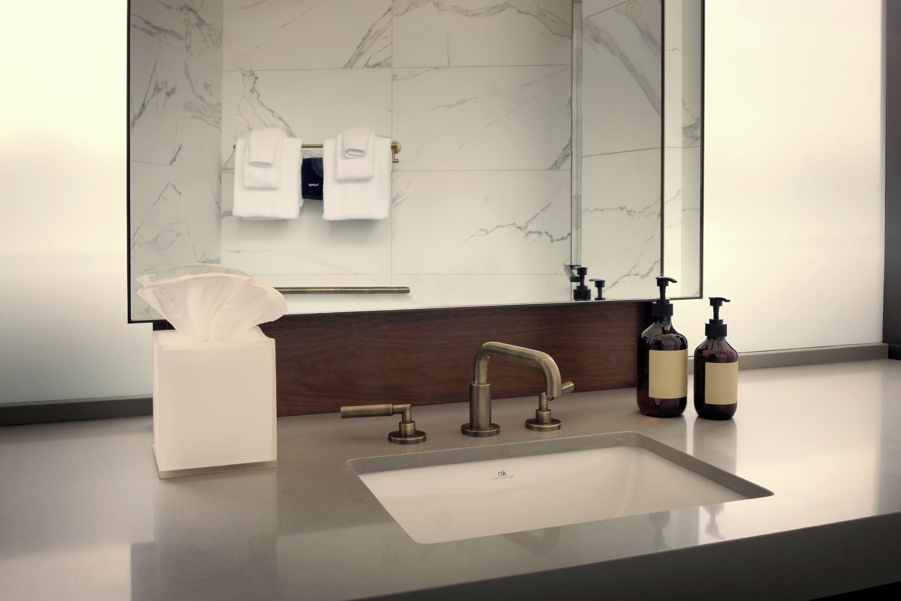 A modern bathroom with a marble backsplash, a white sink, and two soap dispensers.