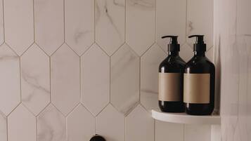 A bathroom with hexagonal marble tiles, a wall-mounted faucet, and two black bottles on a shelf.
