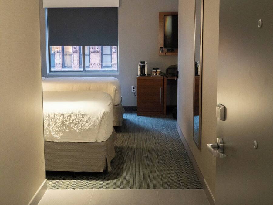 A hotel room with a bed, a small desk, a mirror, and a window.
