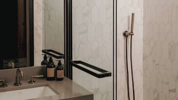 A modern bathroom with a glass-enclosed shower, a large mirror, and a marble-tiled wall.