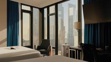 A hotel room with a large bed, a chair, a desk, and a view of tall buildings.