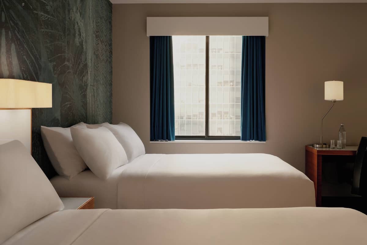 A hotel room with a large bed, a bedside table, a lamp, and a window with curtains.