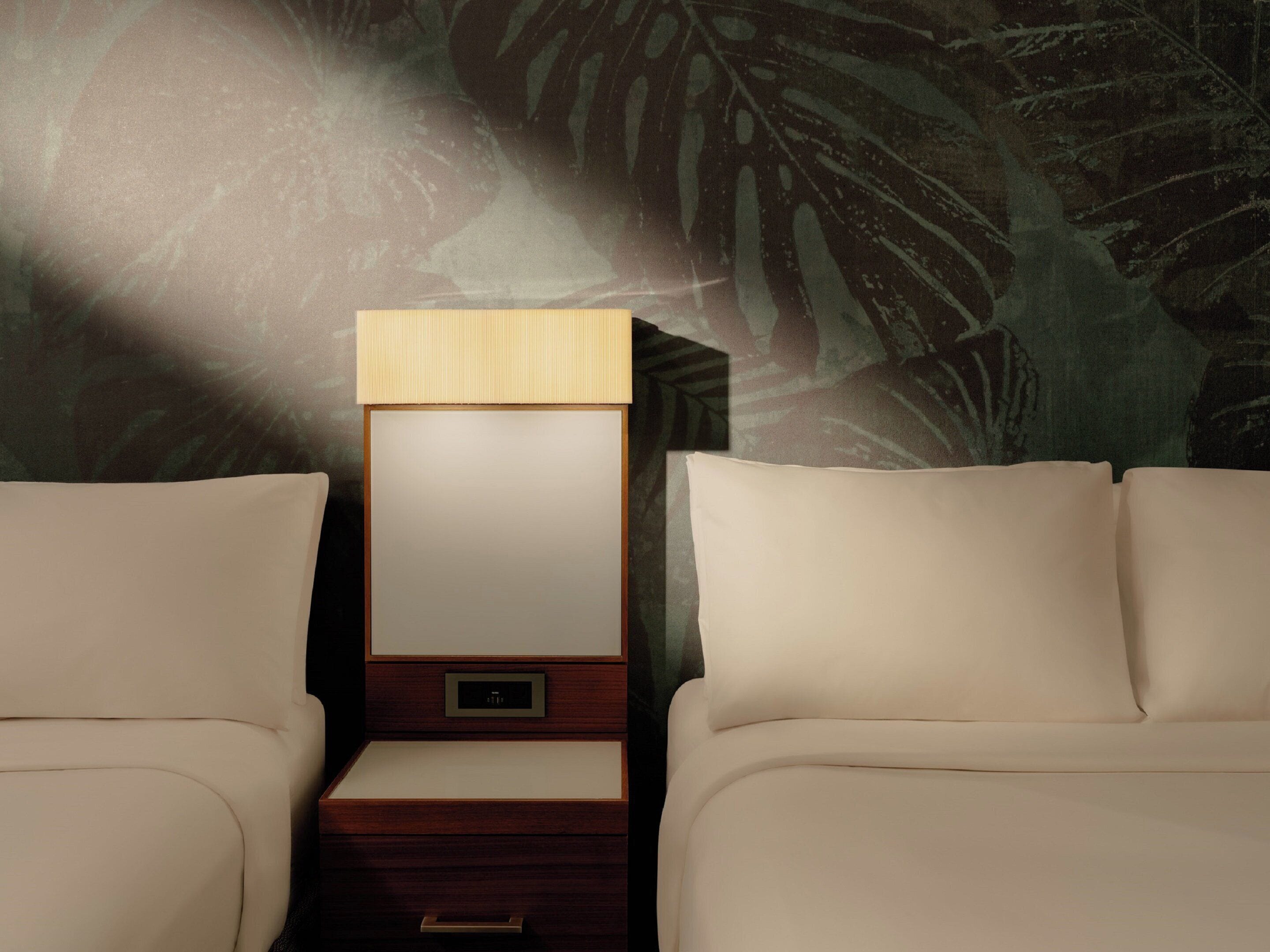 A hotel room with a bed, a nightstand, and a wall with a leaf pattern.