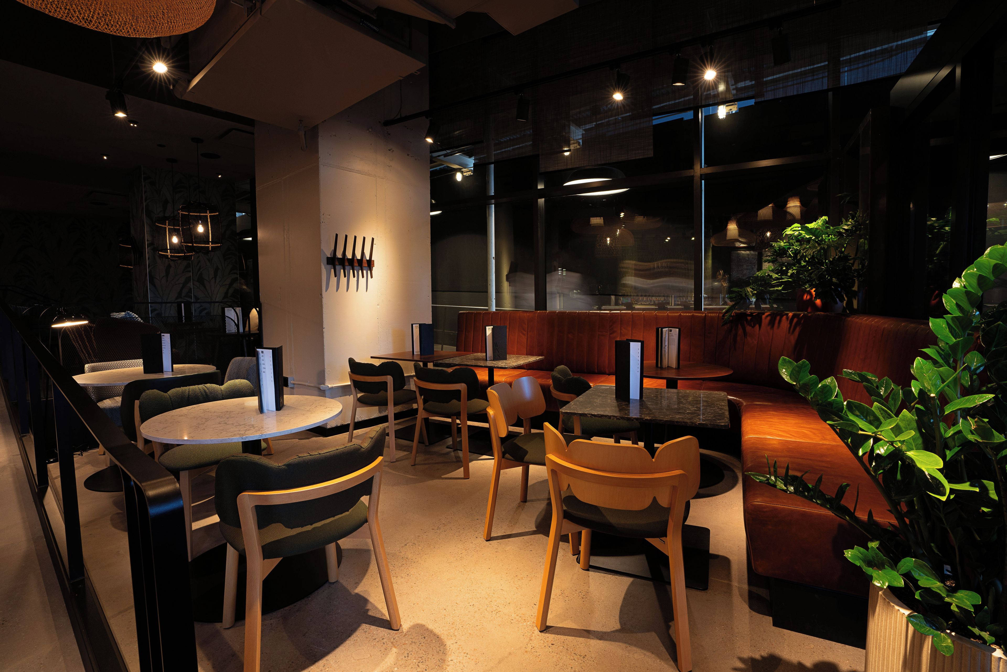 A restaurant interior with round tables, chairs, a bar area, and a seating section with a cushioned bench.