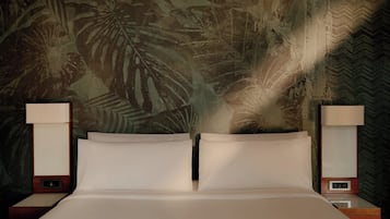 Una cama con dos almohadas, flanqueada por dos mesitas de noche con lámparas, frente a una pared con diseño de hojas tropicales.