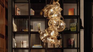Un saló modern amb un sofà de cuir, un butaca blava i una taula de centre de fusta. Un penjall únic penja sobre el sofà, i prestatges plens de llibres i objectes decoratius revesteixen les parets.