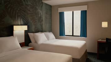 A hotel room with two beds, a window with curtains, a lamp, and a wall with a tropical mural.