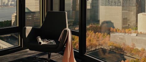 A modern room with a large window, a black chair, and a view of a cityscape with tall buildings.