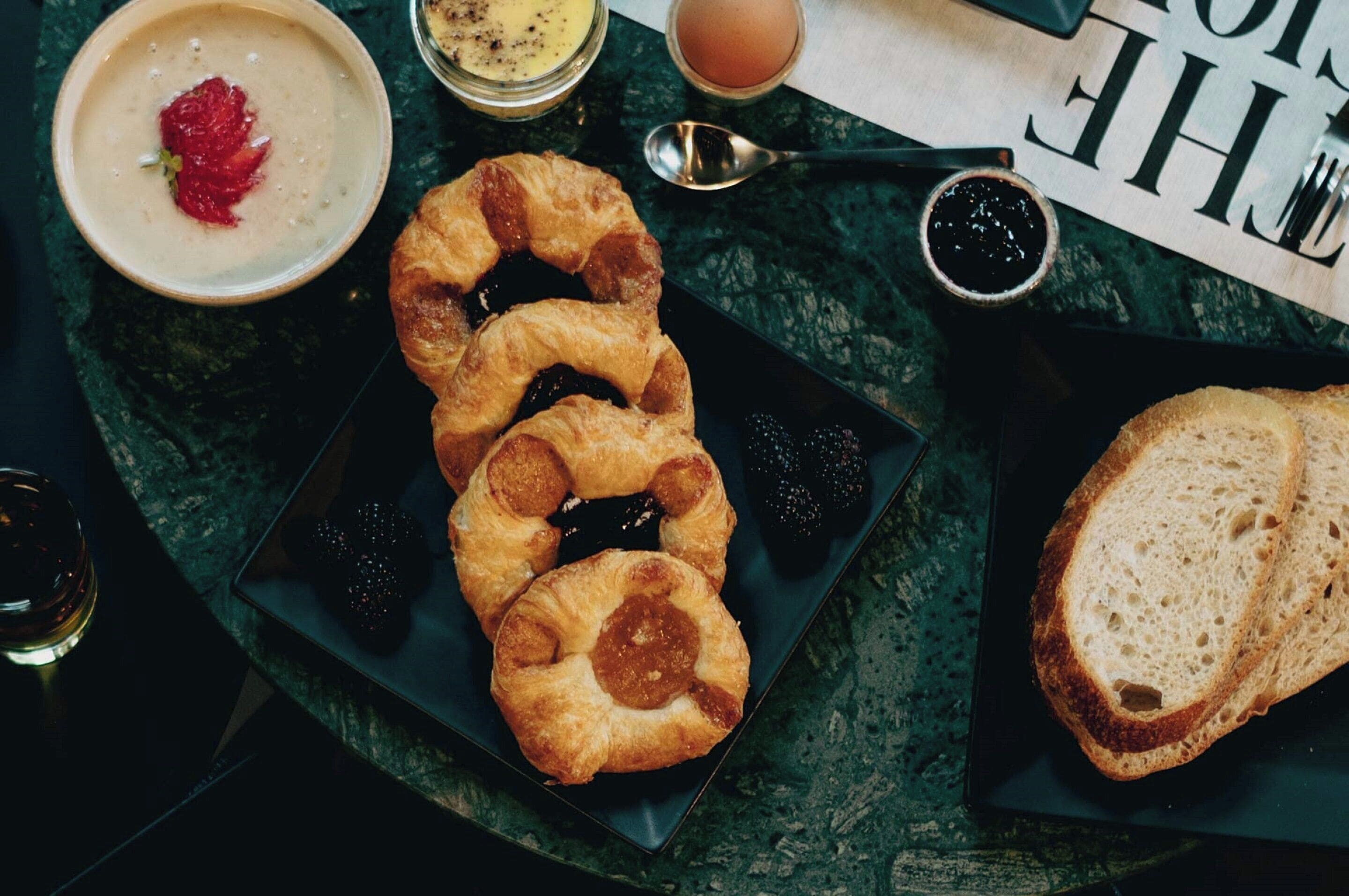 A table with croissants, bread, a bowl of soup, and a cup of coffee.