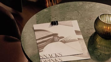 A round table with a menu card labeled "Snacks Drinks" and a small lamp.