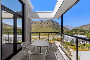 Enjoy breathtaking views of the surrounding mountains from this balcony with a glass door leading to a dining area.