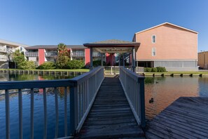 Waterfront property with a bridge leading to a building with a flat roof and red facade, offering multiple balconies.