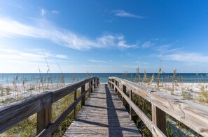 Une promenade en bois qui mène à une plage, avec un ciel dégagé.