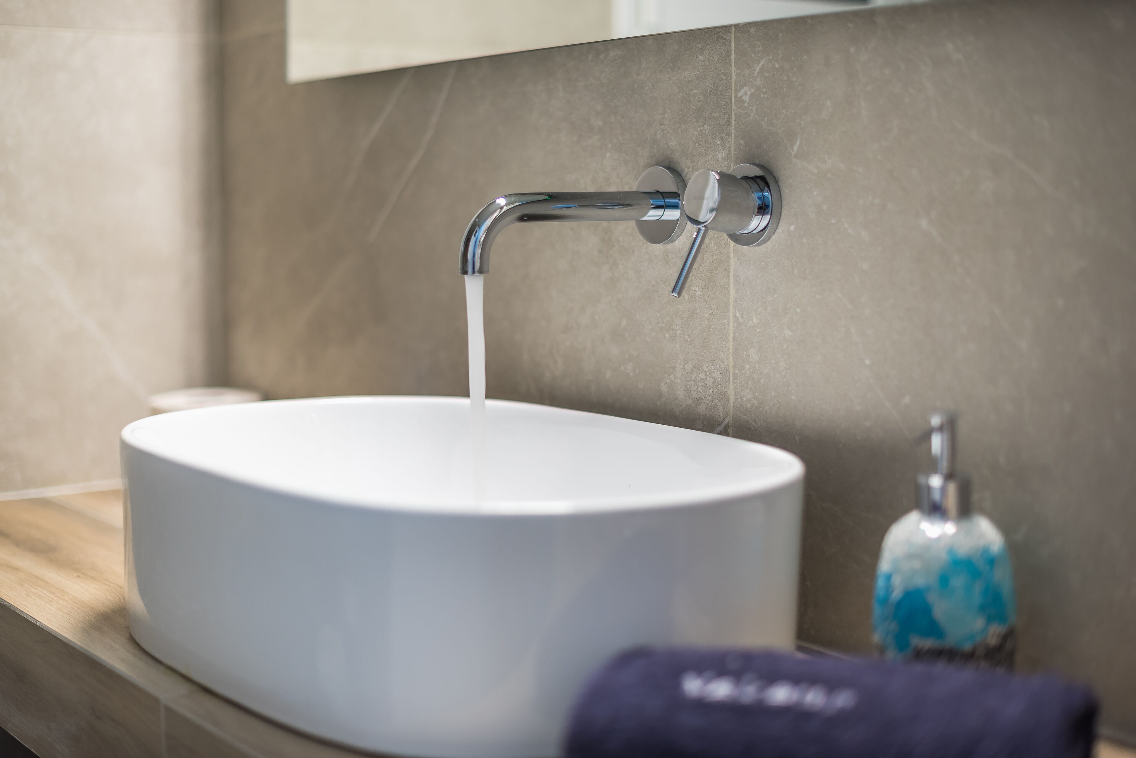 A bathroom sink with running water, a soap dispenser, and a towel on the counter.