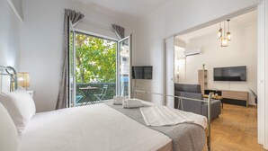 A modern hotel room with a large bed, a balcony with a view of greenery, a flat-screen TV, and a wooden floor. - Athens Bright Suite by Cloudkeys (Athens)