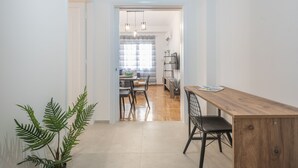 A modern kitchen with a wooden table and chairs, a potted plant, and a view into the dining area. - Athens Bright Suite by Cloudkeys (Athens)